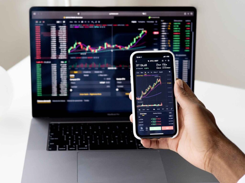 Person holding smart phone with stock markets on screen and laptop